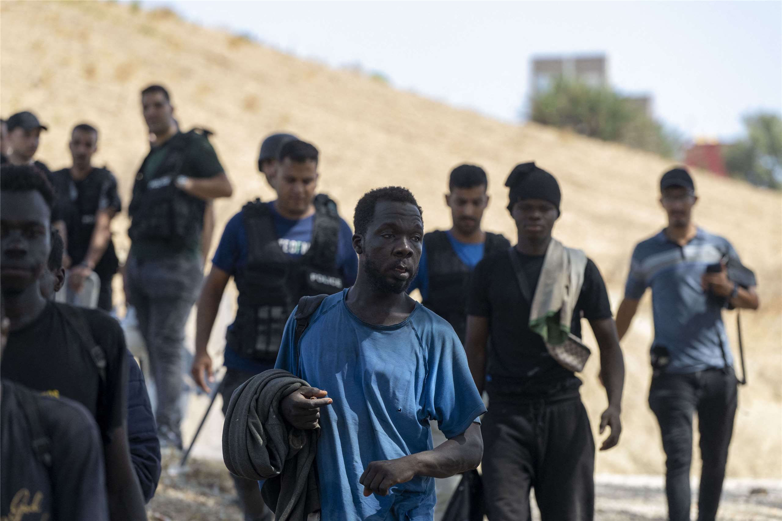 Migrants walk under police escort on a hillside path in Ceuta after crossing from Morocco