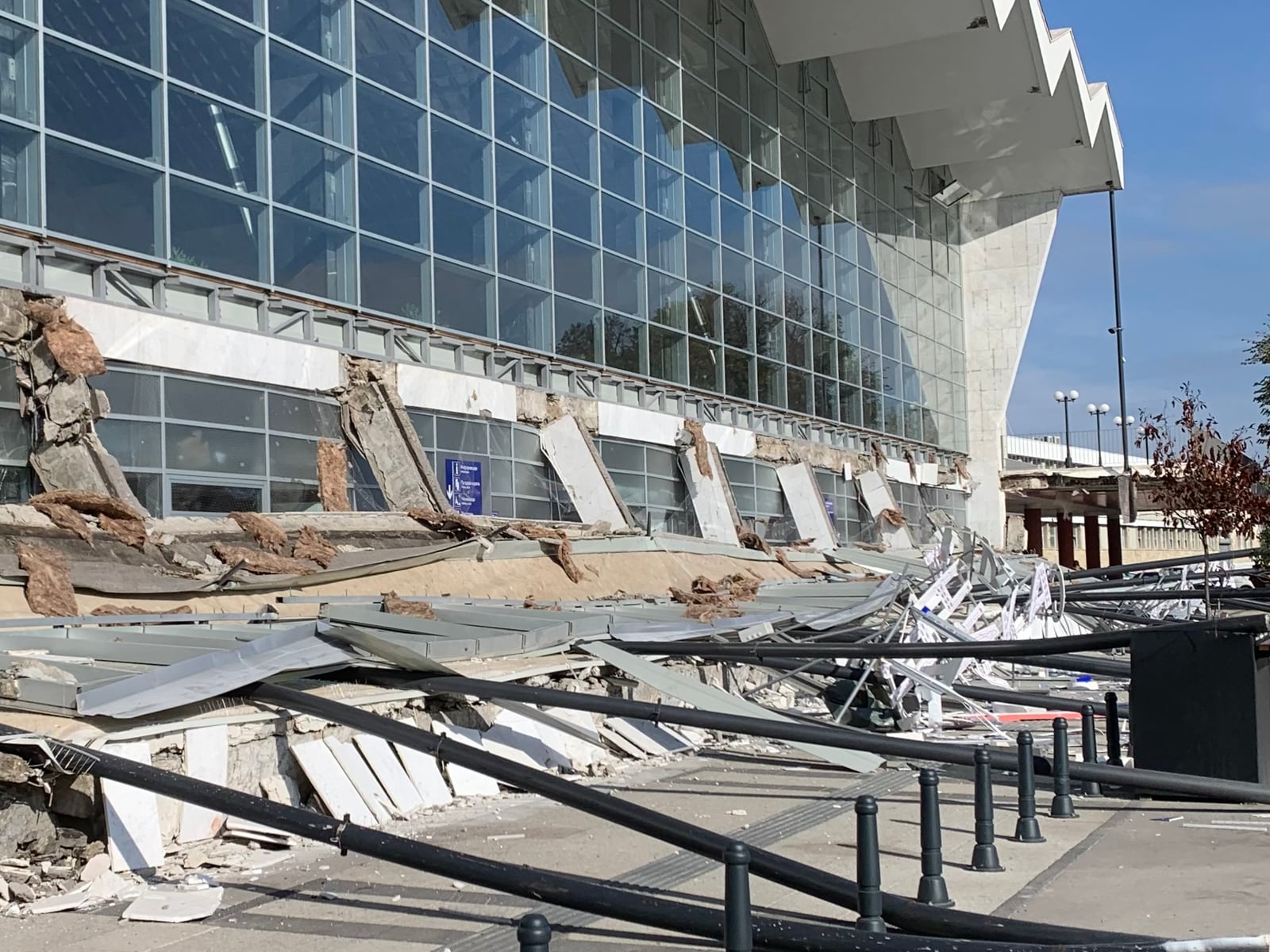 Collapsed concrete canopy and twisted railings lying in front of the glass facade of Novi Sad railway station, minutes after the collapse on 1 November 2024